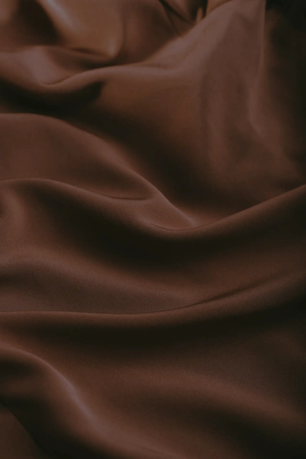 Tela suave en tono chocolate con pliegues cálidos, evocando la búsqueda de ropa cómoda y agradable al tacto para el lipedema